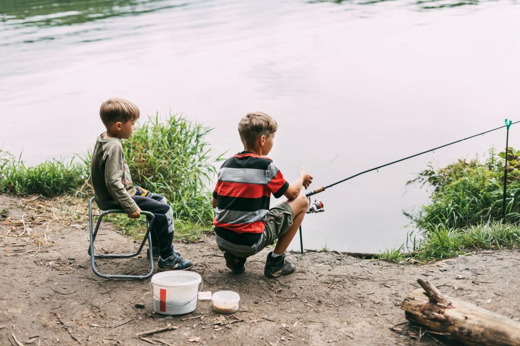 two brothers sit shore lake river fish with fishing rods