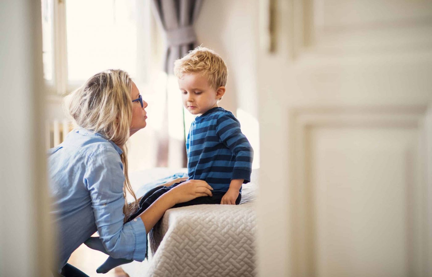 A young mother talking to her toddler son inside in a bedroom. A young mother talking to her sad toddler son inside in a bedroom.